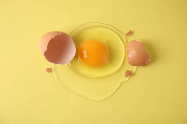 stock image Broken raw egg and shell on yellow background, top view