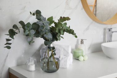 Towels, toiletries and glass vase with beautiful eucalyptus branches on bathroom counter. Interior design