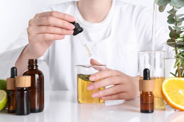 Aromaterapi ürünü. Bilim adamı laboratuarda, yakın planda, beyaz masada gerekli yağları geliştiriyor.