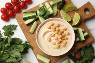 Lezzetli humus, kasede nohut ve ışık masasında taze ürünler.