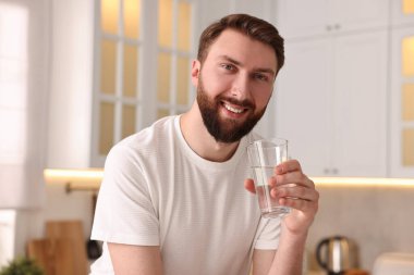 Sabahları mutfakta bir bardak suyla mutlu genç bir adam.