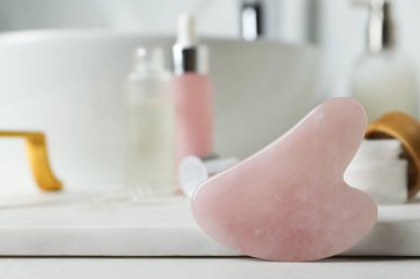 Rose Quartz gua sha aleti ve tuvalet malzemeleri banyodaki beyaz tezgahta, yakın plan. Metin için boşluk