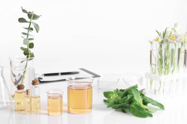 Aromaterapi ürünü. Laboratuvardaki beyaz masanın üzerinde gerekli yağ ve malzemelerle dolu cam eşyalar.