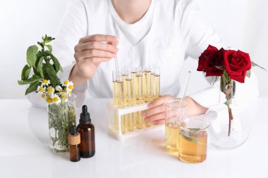Aromaterapi ürünü. Bilim adamı laboratuarda, yakın planda, beyaz masada gerekli yağları geliştiriyor.