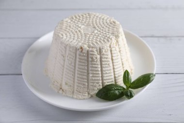 Taze ricotta (krem peynir) ve fesleğen beyaz ahşap masada.