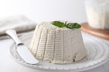 Taze ricotta (krem peynir) fesleğen ve bıçakla beyaz ahşap masada, yakın plan.