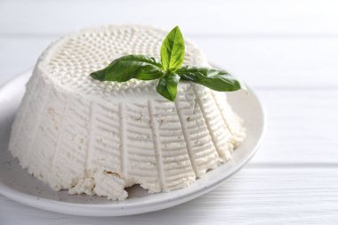 Lezzetli ricotta (krem peynir) ve fesleğen beyaz ahşap masada, yakın plan.