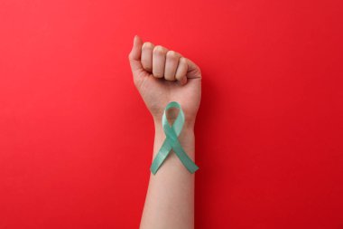 Woman holding turquoise awareness ribbon on red background, top view clipart