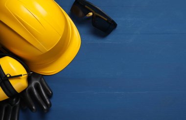 Kasket, kulaklık, koruyucu eldivenler ve mavi ahşap arka planda gözlükler, düz yatış. Metin için boşluk