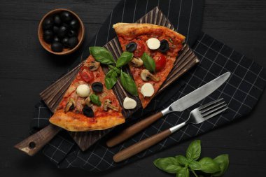 Pieces of tasty pizza served on black wooden table, flat lay