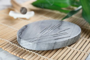 Bambu hasırında akupunktur iğneleri olan gri taş bardak altlığı, yakın plan.