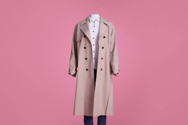Pembe arka planda şık bir ceket, kot pantolon ve gömlek giymiş bir kadın manken.