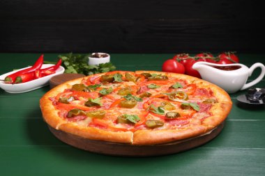 Lezzetli pizza Diablo, malzemeler ve yeşil ahşap masa keskisi.