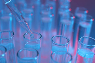 Renk arka planında pipetten test tüpüne sıvı damlatılıyor, yakın plan