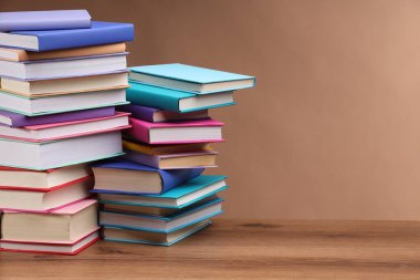 Açık kahverengi arkaplan ile ahşap masa üzerinde renkli kitap yığınları, metin için boşluk