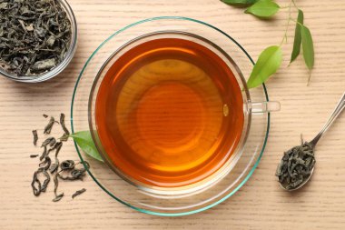 Fincanda taze yeşil çay, kaşık ve yapraklar ahşap masa, düz uzanmış