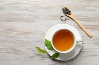 Yeşil çayı fincanda, kaşıkta ve yapraklarda hafif ahşap masada, düz yerde serinletiyor. Metin için boşluk