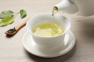 Ahşap masada fincana serinletici yeşil çay dökülüyor, yakın plan.