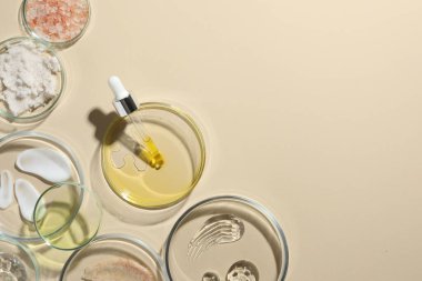 Bej arka planda farklı kozmetik ürünleri olan petri kapları, düz yatak. Metin için boşluk