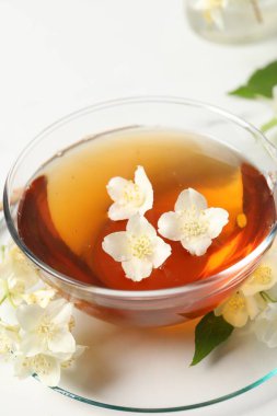 Sıcak yasemin çayı fincanda ve çiçekler beyaz mermer masada.