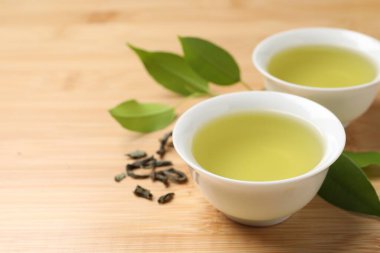 Yeşil çayı fincanlarda ve yaprakları ahşap masada serinletiyor, yakın plan. Metin için boşluk