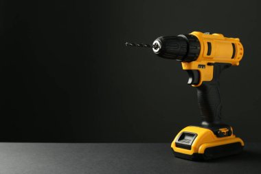 Gri masadaki modern kablosuz elektrikli matkap siyah arkaplana karşı. Metin için boşluk