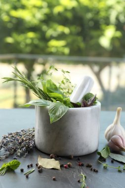 Değişik aromatik otlar, gri masa üzerinde kabuklu havan ve baharatlar.