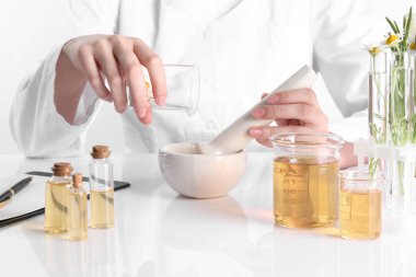 Aromaterapi ürünü. Bilim adamı laboratuarda, yakın planda, beyaz masada gerekli yağları geliştiriyor.