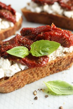 Lezzetli ricotta bruschetta, güneşte kurutulmuş domates ve tabakta fesleğen, yakın plan.