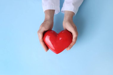 Doktor açık mavi arkaplanda kırmızı kalbi tutuyor.