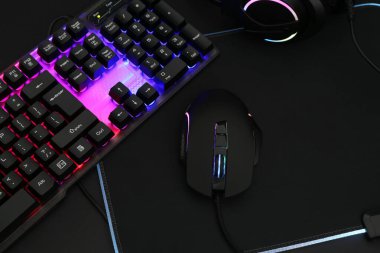 Koyu arkaplanda bilgisayar faresi, kulaklık ve RGB klavyesi, üst görünümde