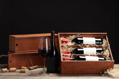 İçinde şarap şişeleri, cam, mantar ve tirbuşon olan kutu siyah arka planda.