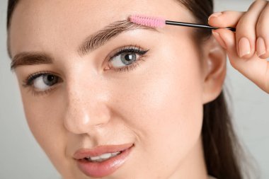 Arka planda tüyler ürpertici fırçası olan genç bir kadın, yakın plan. Kaş düzeltmesi.