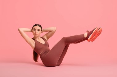 Genç bir kadın pembe arka planda aerobik egzersizi yapıyor.