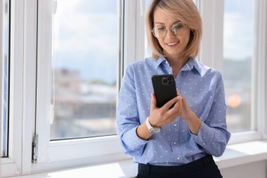 Pencerenin yanında cep telefonu kullanan mutlu bir kadın, mesaj için boşluk