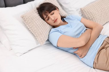 Evde karın ağrısı çeken üzgün bir kadın var.