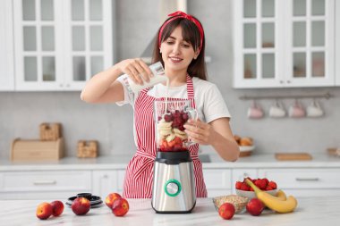 Genç bir kadın mutfaktaki beyaz mermer masada blender ile nefis smoothie yapıyor.