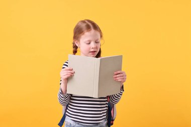 Sarı arka planda kitap okuyan sevimli küçük kız.