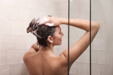 Woman washing hair while taking shower at home, back view