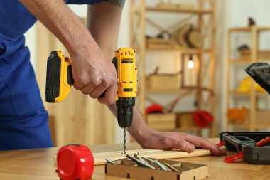 Zanaatkar atölyedeki ahşap masada matkapla çalışıyor.