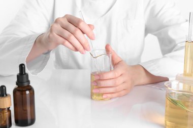 Aromaterapi ürünü. Bilim adamı laboratuarda, yakın planda, beyaz masada gerekli yağları geliştiriyor.