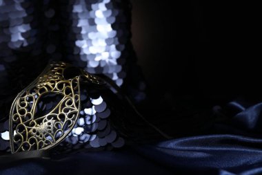 Karanlığın içinde altın pullu güzel bir karnaval maskesi ve kumaş, yakın plan. Metin için boşluk