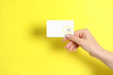 Sarı arka planda SIM kartı tutan kadın, yakın plan. Metin için boşluk