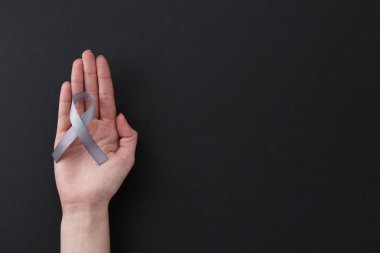 Siyah arka planda gri farkındalık kurdelesi olan bir kadın. Metin için boşluk