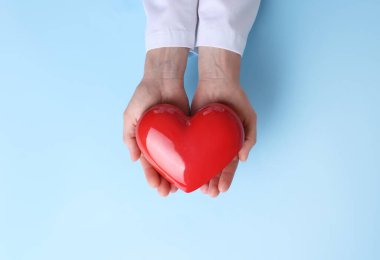 Doktor açık mavi arkaplanda kırmızı kalbi tutuyor.