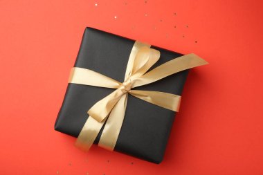 Altın saten yay ve mercan zemin üzerinde konfeti ile hediye kutusu, üst görünüm