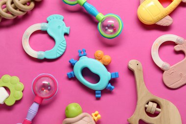 Different baby rattles on pink background, flat lay clipart