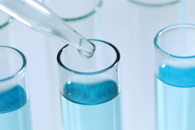 Işık arka planında pipetten test tüpüne sıvı damlatılıyor, yakın plan