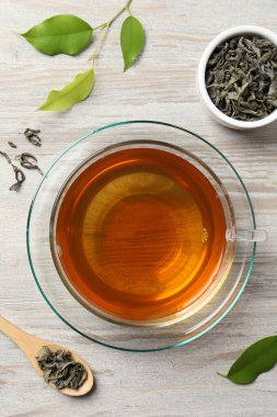 Fincanda yeşil çay, kaşık ve yapraklar hafif ahşap masa, düz uzanmış