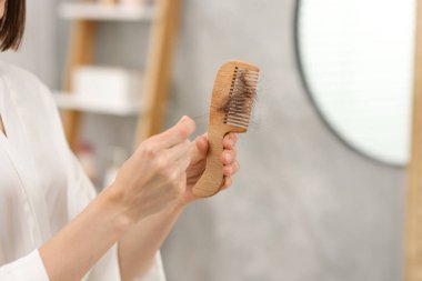 Woman taking her lost hair from comb at home, closeup. Alopecia problem
